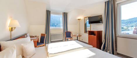 A hotel room with two beds, a desk, a chair, a TV, and a view of the city.