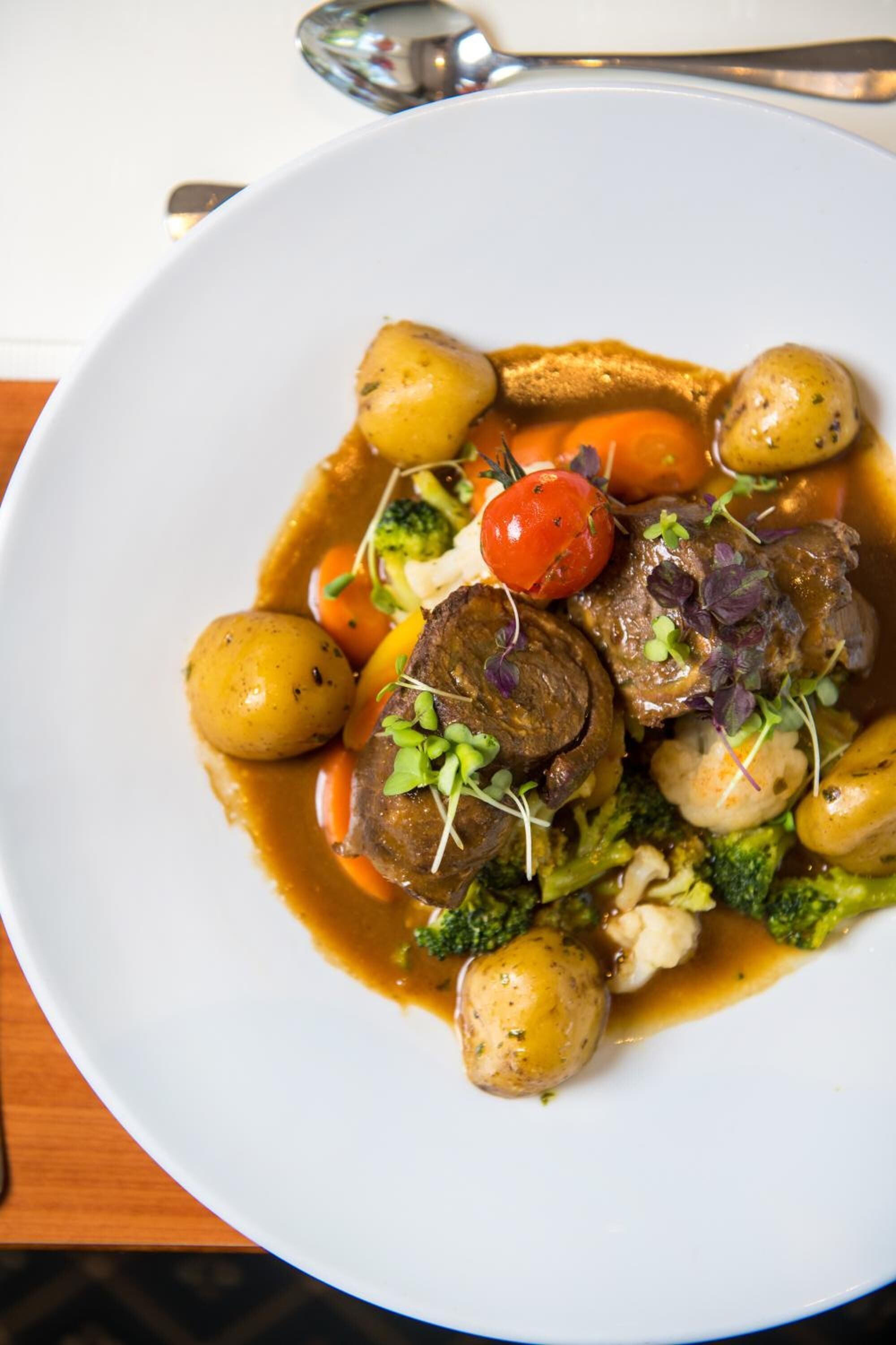 Un plato blanco con carne, verduras y salsa.