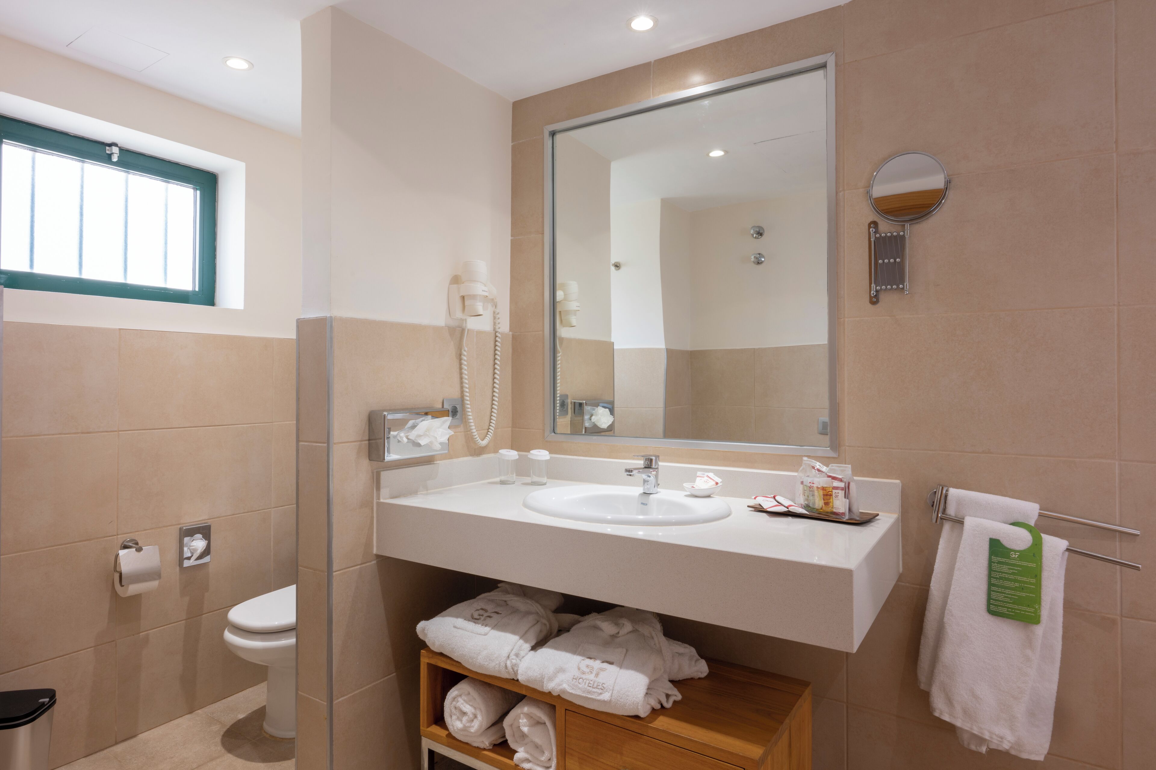 Un bany modern amb un mirall gran, un lavabo i una dutxa. Hi ha tovalloles i productes de tocador al taulell.
