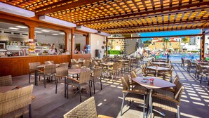 An outdoor cafe area with wicker furniture and a pool in the background. - GF Isabel (Adeje)