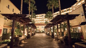 A nighttime view of a hotel corridor with palm trees and wooden pergolas. - GF Isabel (Adeje)