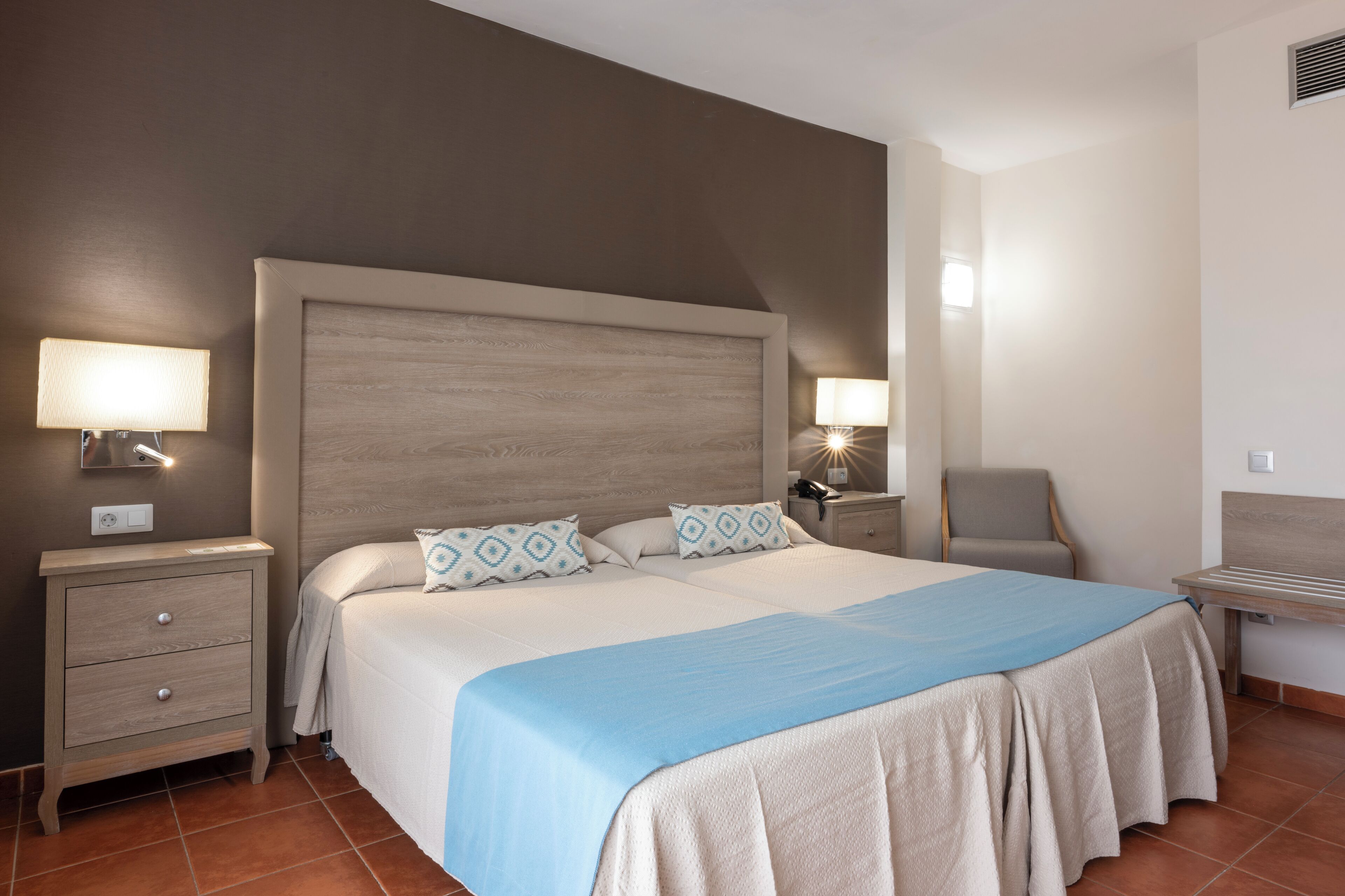 Una habitación de hotel con una cama grande, dos mesitas de noche, una silla y un escritorio.