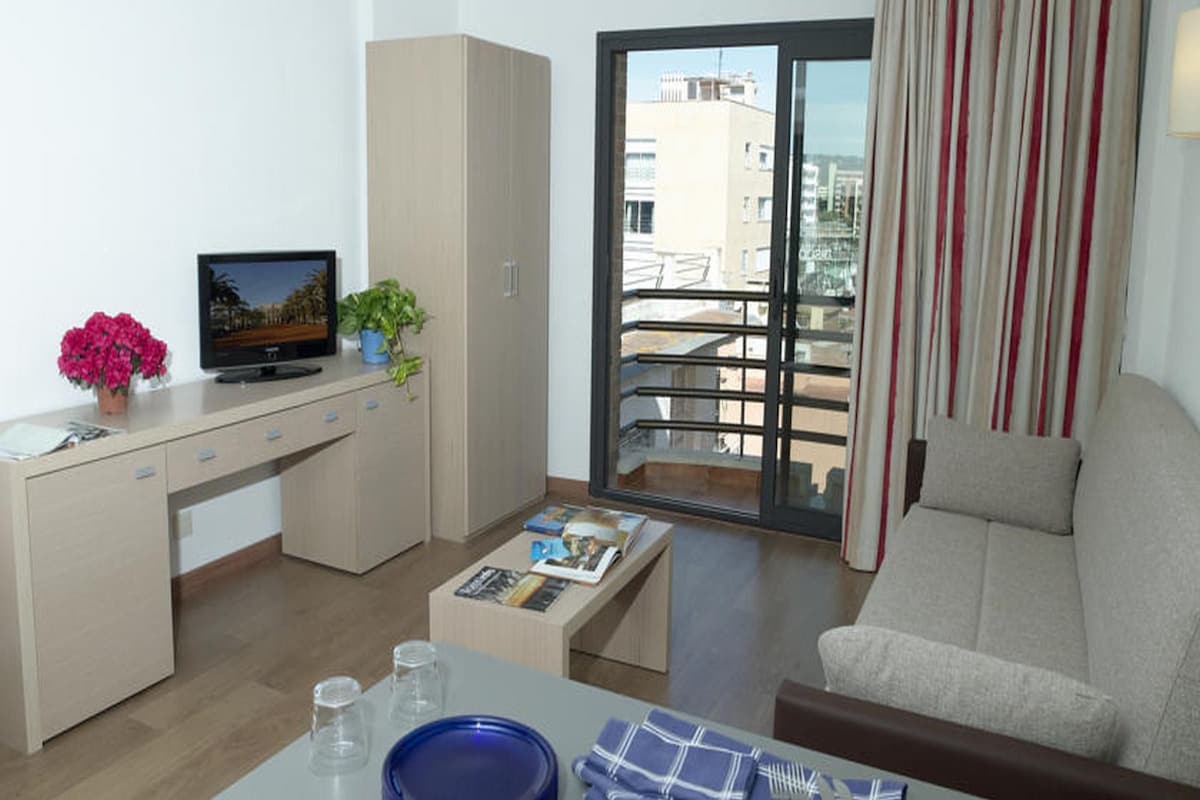 Ein modernes Wohnzimmer mit einer Couch, einem Couchtisch, einem Fernseher und einem Balkon mit Blick auf Gebäude.