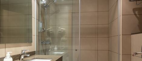 A modern bathroom with a glass-enclosed shower, a large mirror, a sink with a soap dispenser, and a toilet.