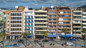 A multi-story hotel with balconies, a parking area, and a beach in the foreground. - Almirall Apartaments (Lloret de Mar)