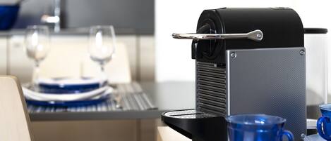 Una cafetera sobre una encimera de cocina, con una taza y platillo azules.