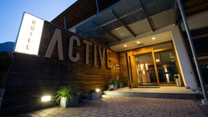 Entrada de un hotel con un cartel que dice "HOTEL ACTIV HOTEL" y un diseño moderno con paneles de madera y plantas en macetas.