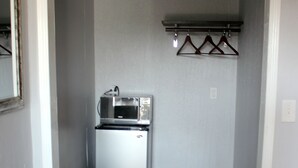 A compact kitchenette with a microwave and refrigerator, a small trash bin, and a coat rack with hangers. - Garden View Inn (Fresno)