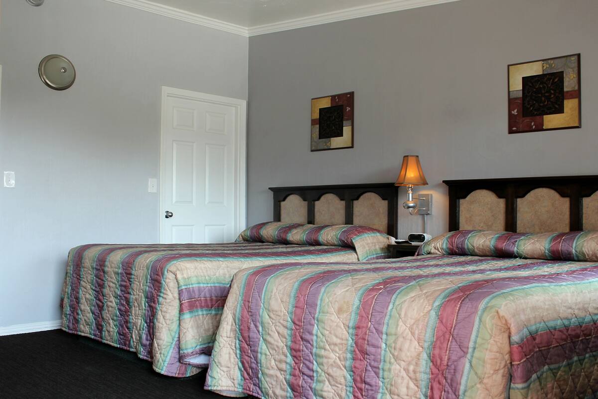 Une chambre d’hôtel avec deux lits, une porte, une table de chevet avec une lampe et deux œuvres d’art murales.