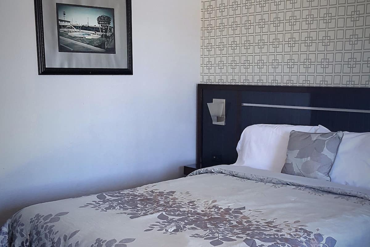 Un lit bien fait, recouvert d’une couvre-lit à motifs floraux, une image encadrée accrochée au mur et un papier peint à motifs au-dessus du lit.