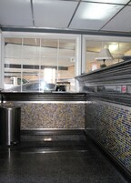 Una estación de metro con paredes de azulejos, un cubo de basura metálico y vistas de coches estacionados afuera.