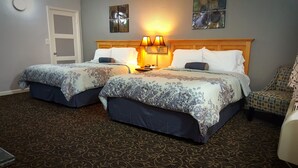 A hotel room with two beds, a wooden headboard, a patterned carpet, and a chair. - Garden View Inn (Fresno)