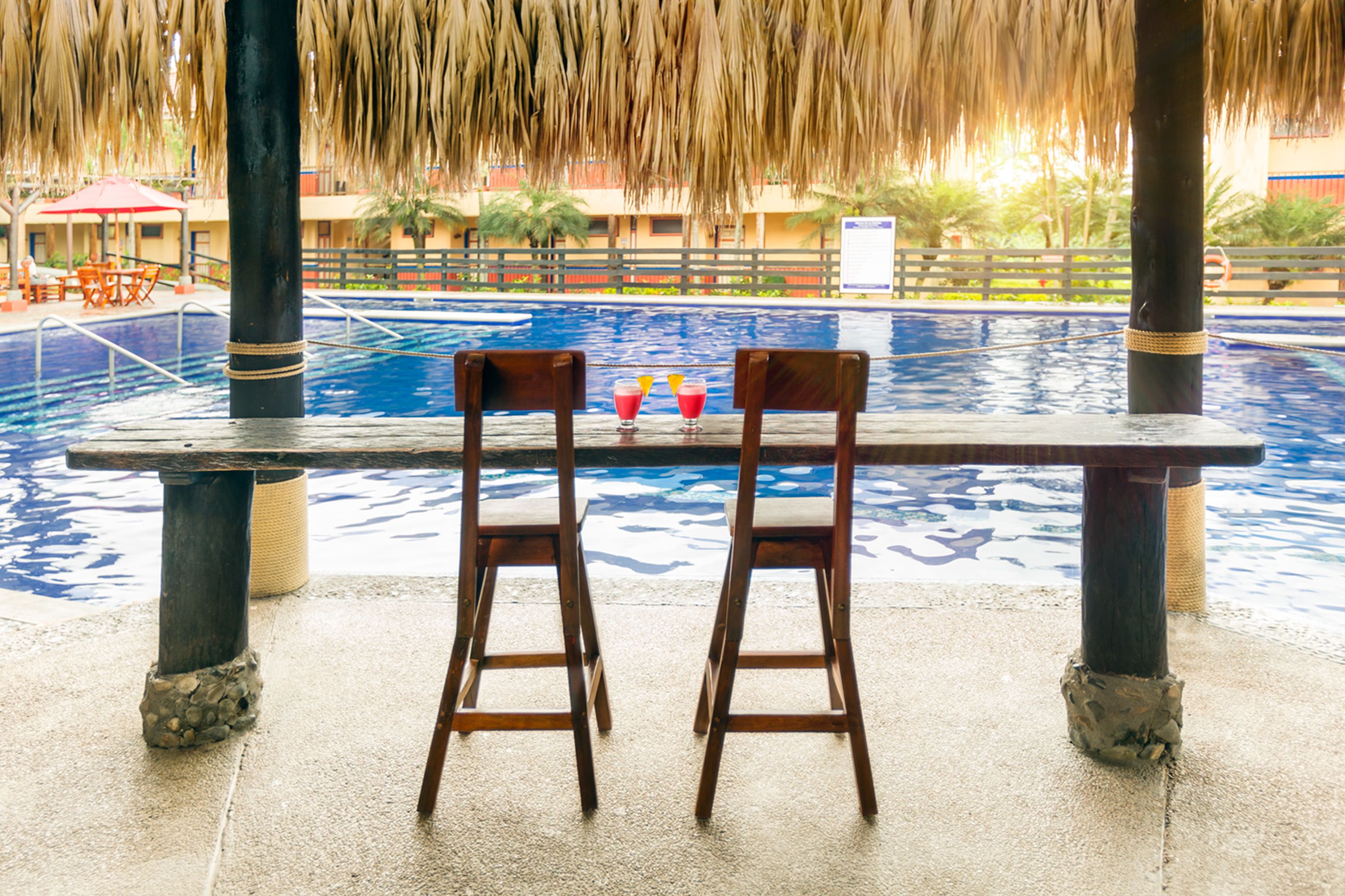 A poolside bar with two wooden chairs and a table, overlooking a swimming pool.