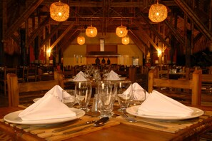 A dining area with wooden tables set for a meal, featuring clear glassware and white napkins.