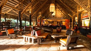 A spacious indoor area with high ceilings and bamboo beams, furnished with wooden benches and tables, and a bar area in the background. - Decameron Panaca All Inclusive (Quimbaya)