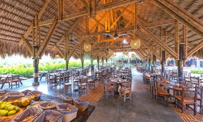 An indoor dining area with bamboo structures, tables, chairs, and baskets of fruits. - Decameron Panaca All Inclusive (Quimbaya)