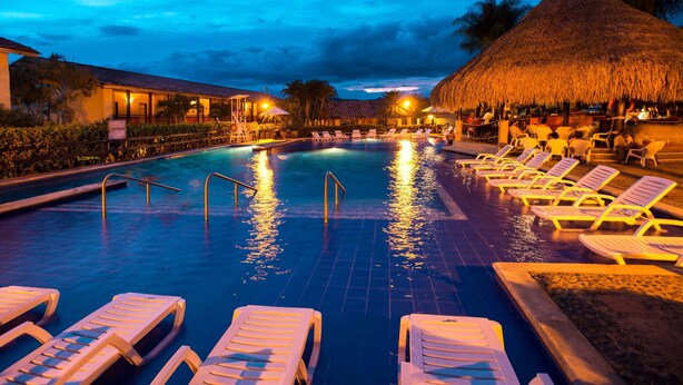 A swimming pool with lounge chairs and a thatched-roof structure. - Decameron Panaca All Inclusive (Quimbaya)