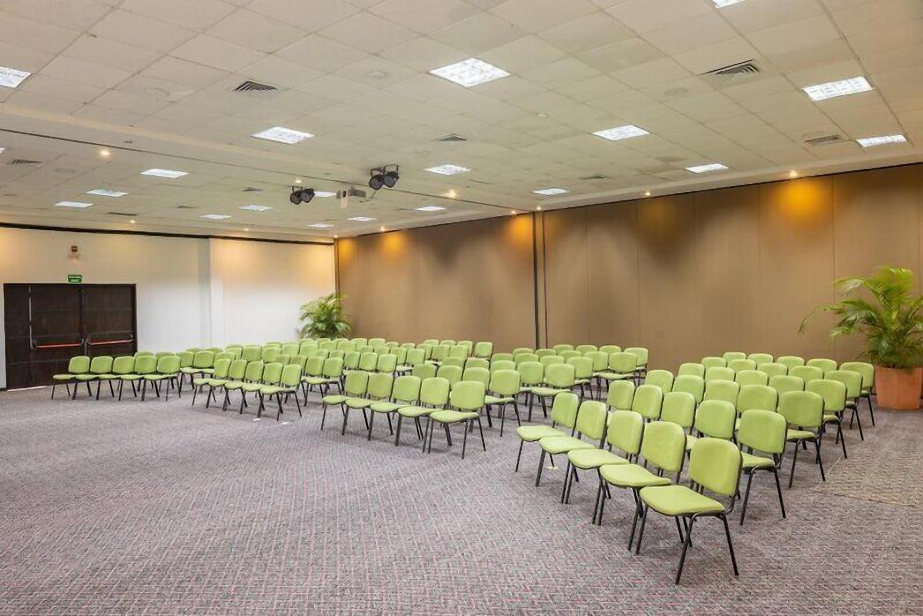 A conference room with rows of chairs, a projector screen, and a carpeted floor.