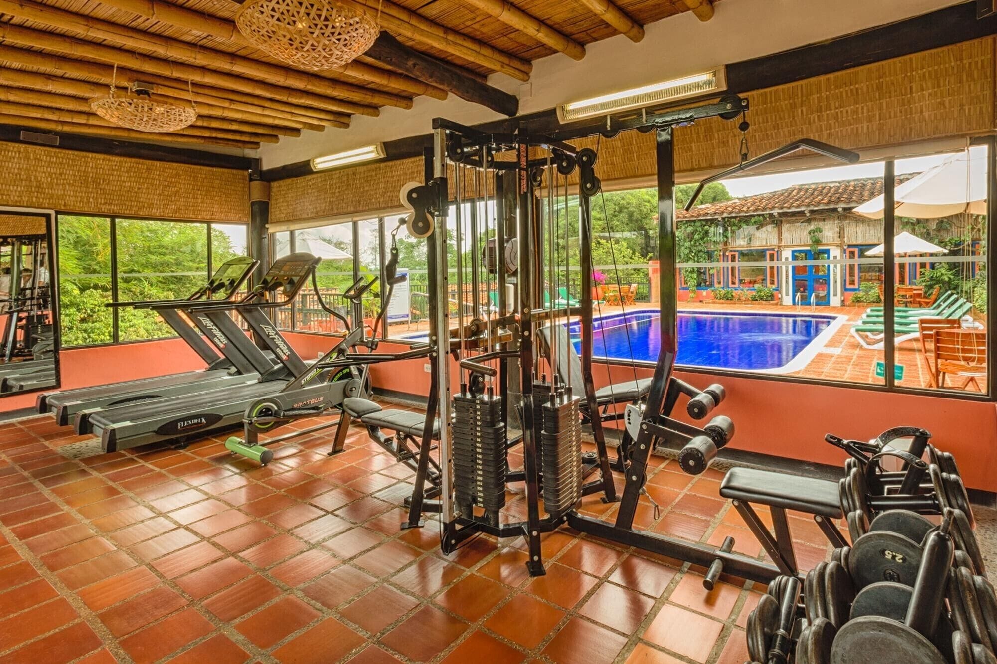 Un gimnasio con equipo de ejercicio, una cinta de correr y vistas a una piscina exterior.