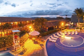 A hotel pool area with lounge chairs, a lifeguard chair, and a thatched-roof building.