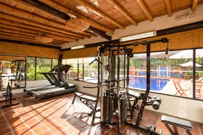 Un gimnasio con equipo de ejercicio, una cinta de correr y vistas a una piscina exterior.
