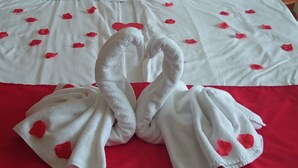 A bed with white linens and red rose petals, and two towels shaped like swans. - Rudolf Hotel Hajdúszoboszló (Hajduszoboszlo)