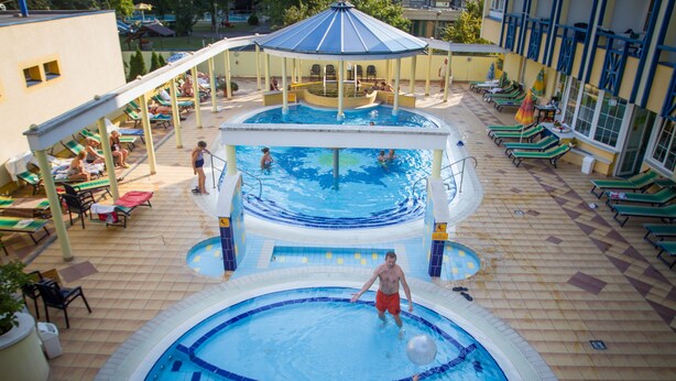 A pool area with multiple swimming pools, sun loungers, and a covered seating area. - Rudolf Hotel Hajdúszoboszló (Hajduszoboszlo)