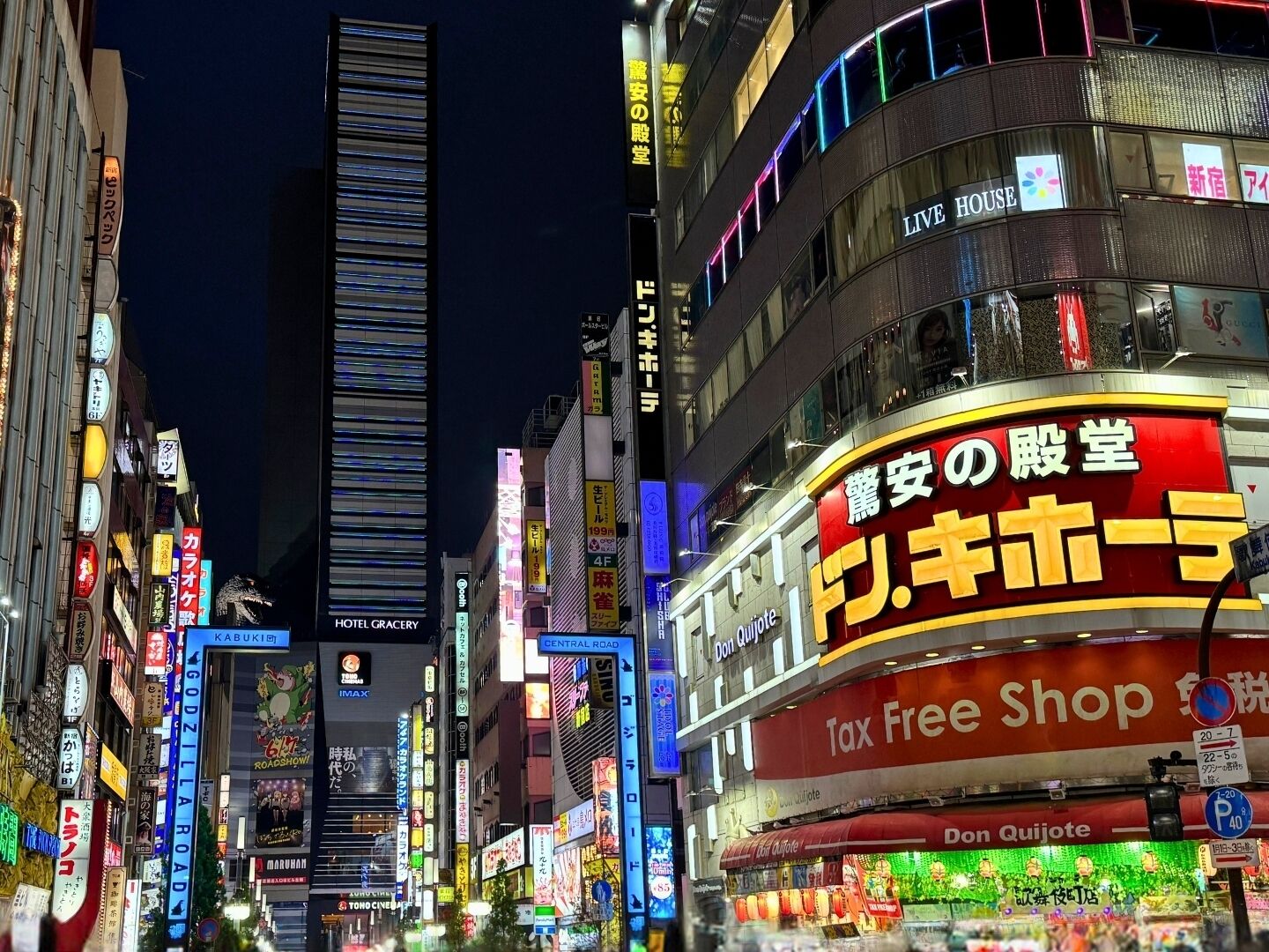 Une rue animée d’une ville, de nuit, avec des enseignes lumineuses, dont une grande enseigne indiquant « Boutique hors taxes ».
