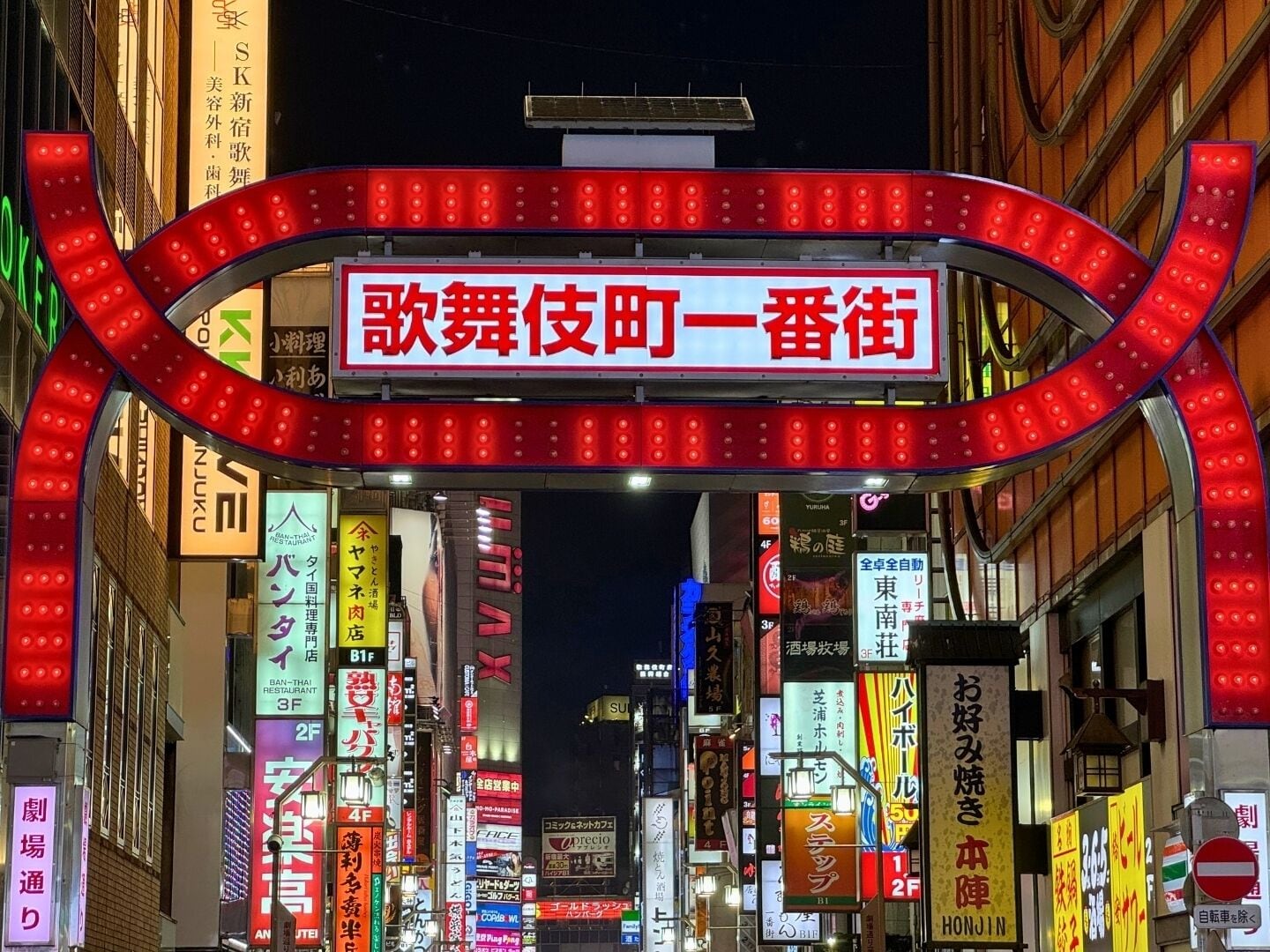 A brightly lit street with numerous neon signs in a foreign language, indicating a vibrant urban area.