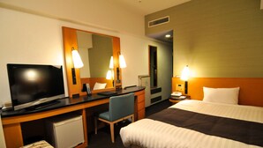 Una camera d'albergo con un letto, una scrivania con una sedia, una televisione e un piccolo frigorifero.