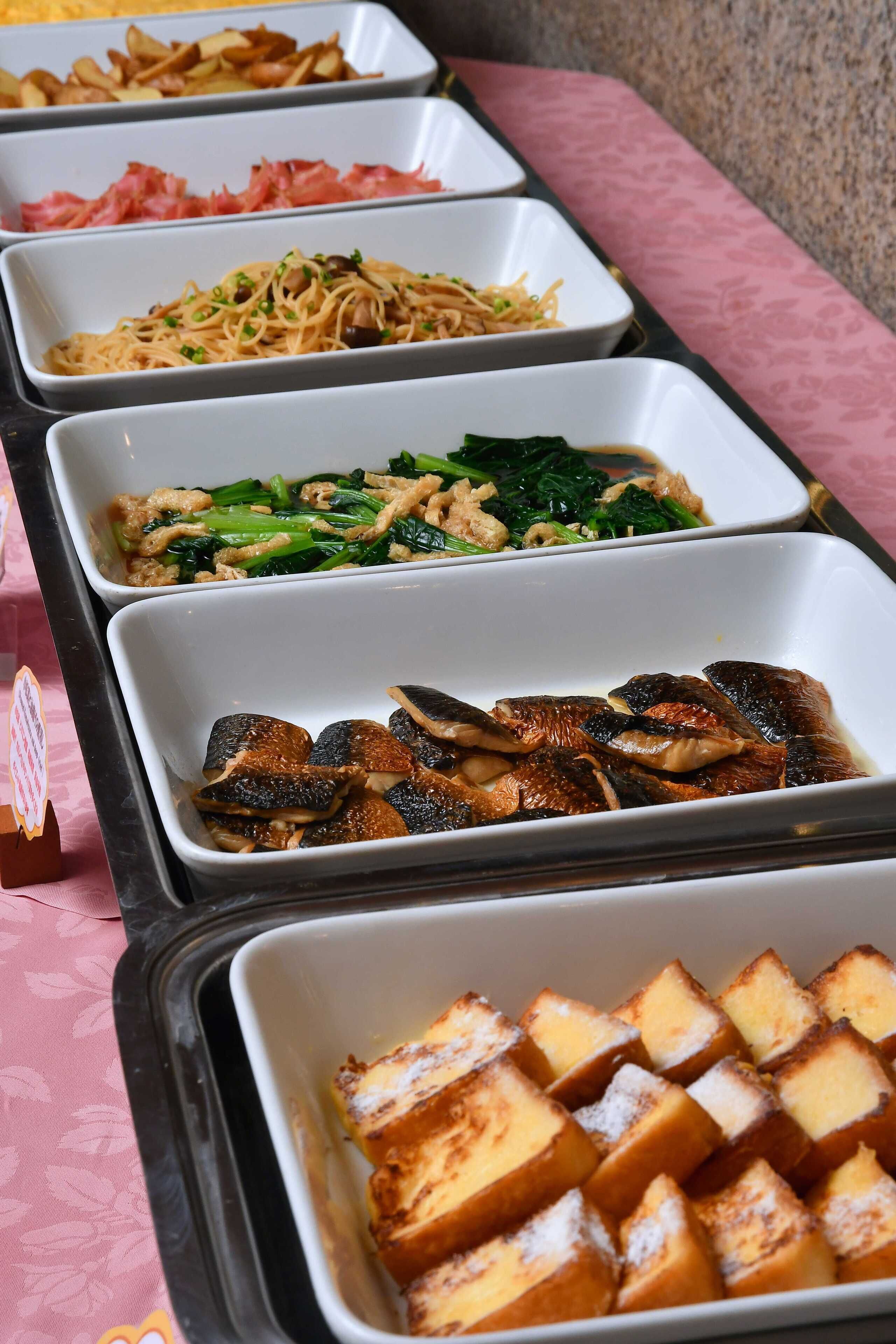 A buffet with various dishes including noodles, greens, mushrooms, and bread.