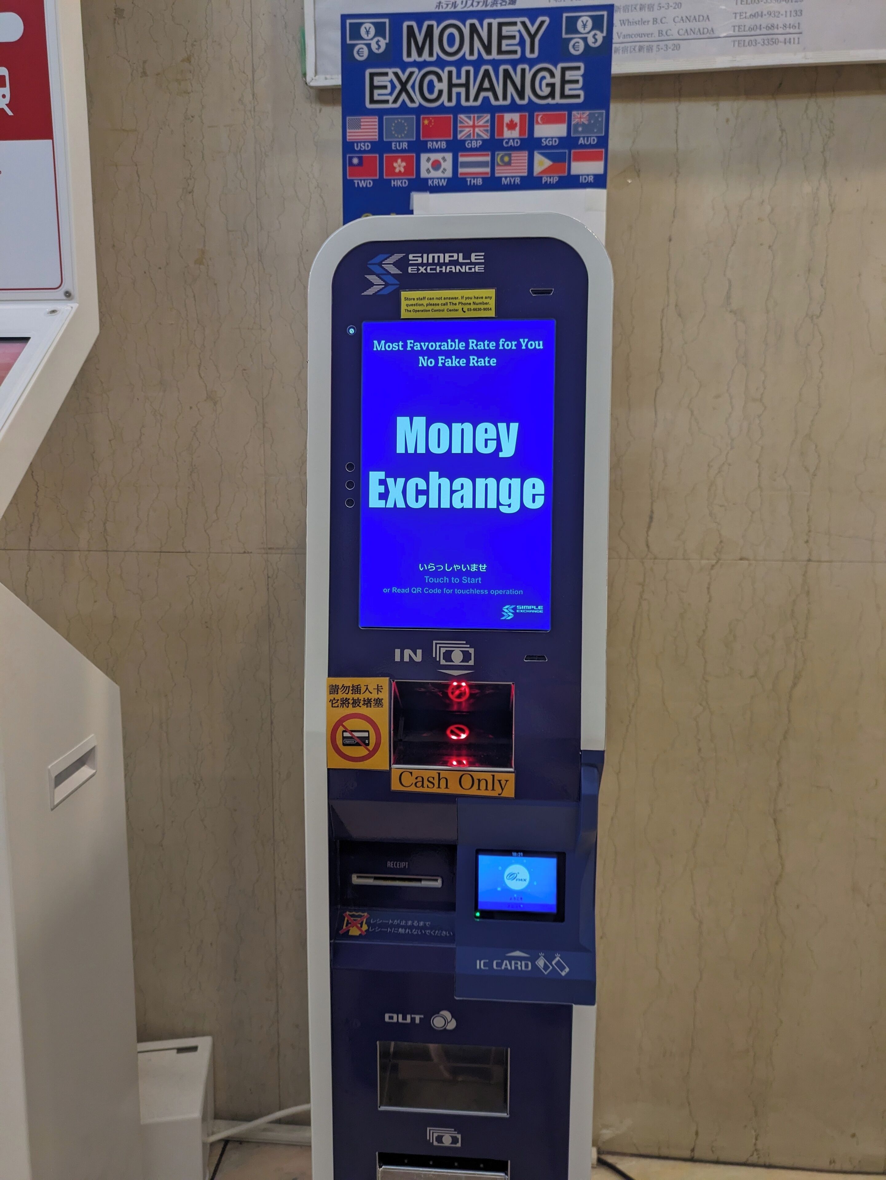 A money exchange machine with a digital screen displaying 'Money Exchange' and a sign above it listing various currencies.