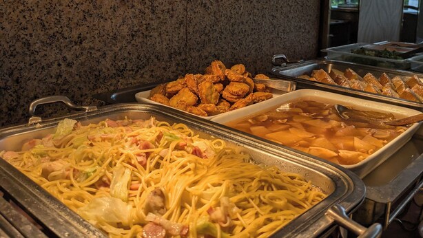 Un buffet con diversi piatti, tra cui noodles, cibi fritti e una zuppa.