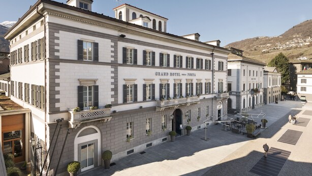 A large, historic building with a sign reading "Grand Hotel Posta." It features a prominent entrance with a covered walkway, multiple windows, and a flat roof. - Grand Hotel della Posta, WorldHotels Distinctive (Sondrio)