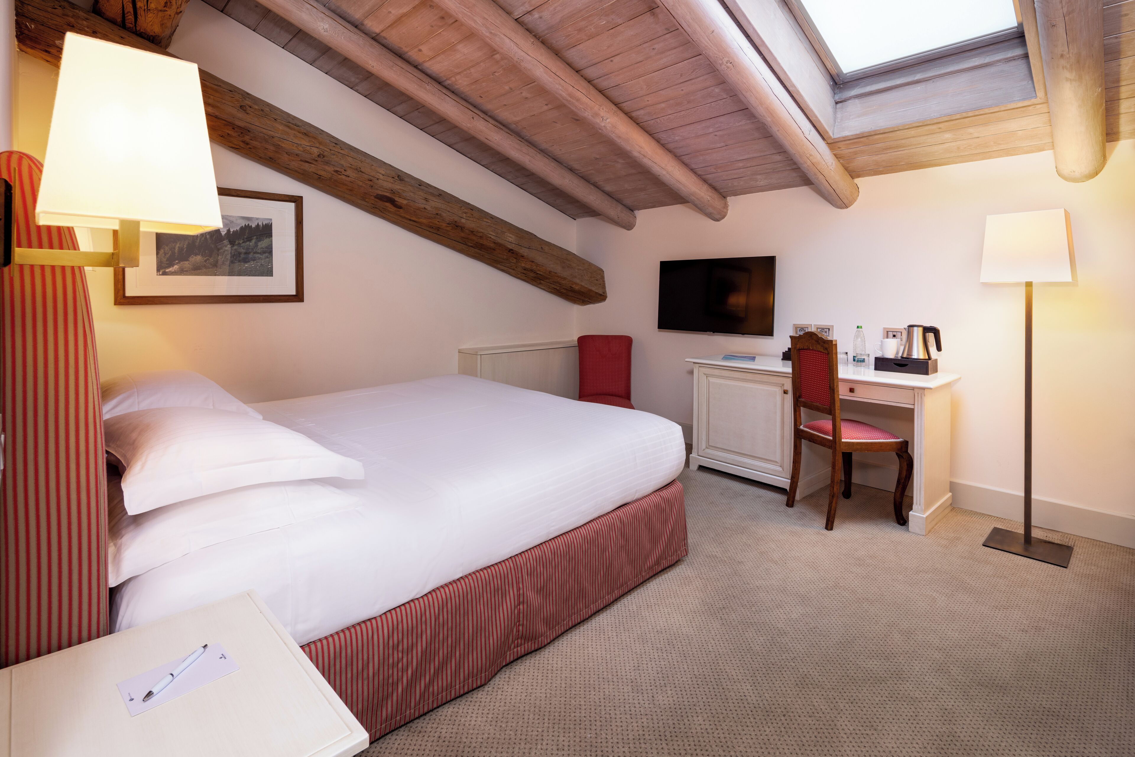A hotel room with a large bed, a desk, a chair, a flat-screen TV, and a skylight.