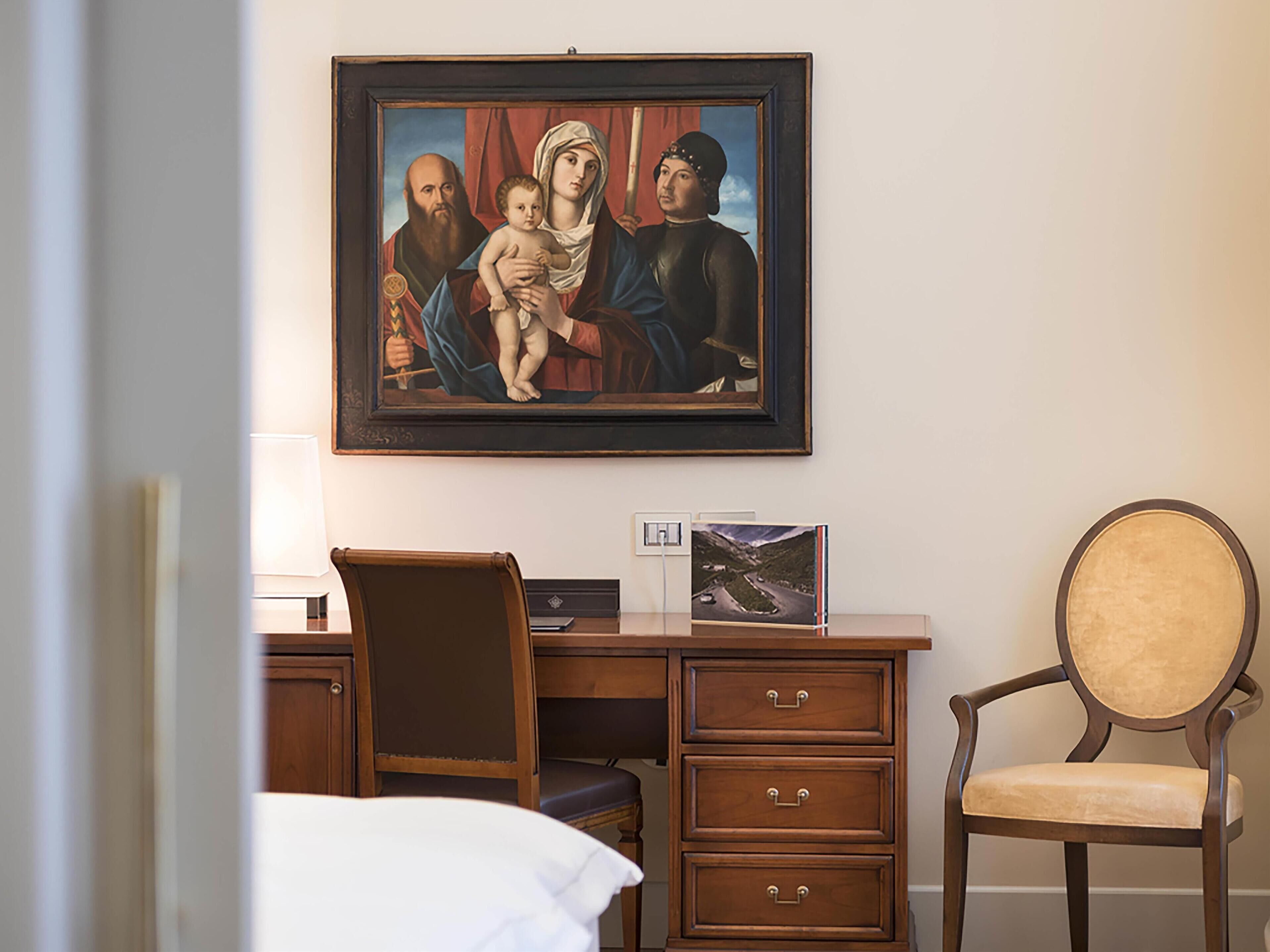Una camera d'albergo con un letto, una scrivania con una sedia, un quadro incorniciato e un comodino con una lampada.