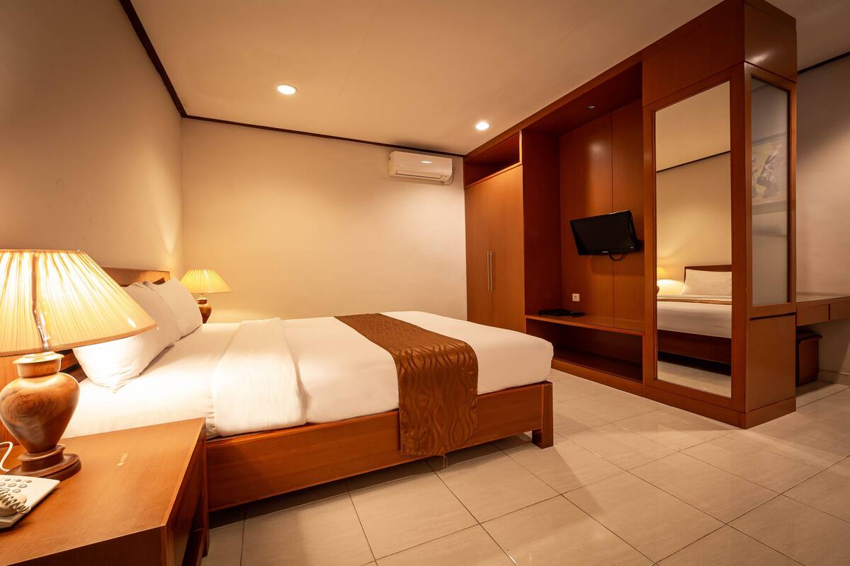 A hotel room with a bed, bedside lamps, a TV, and a mirror.
