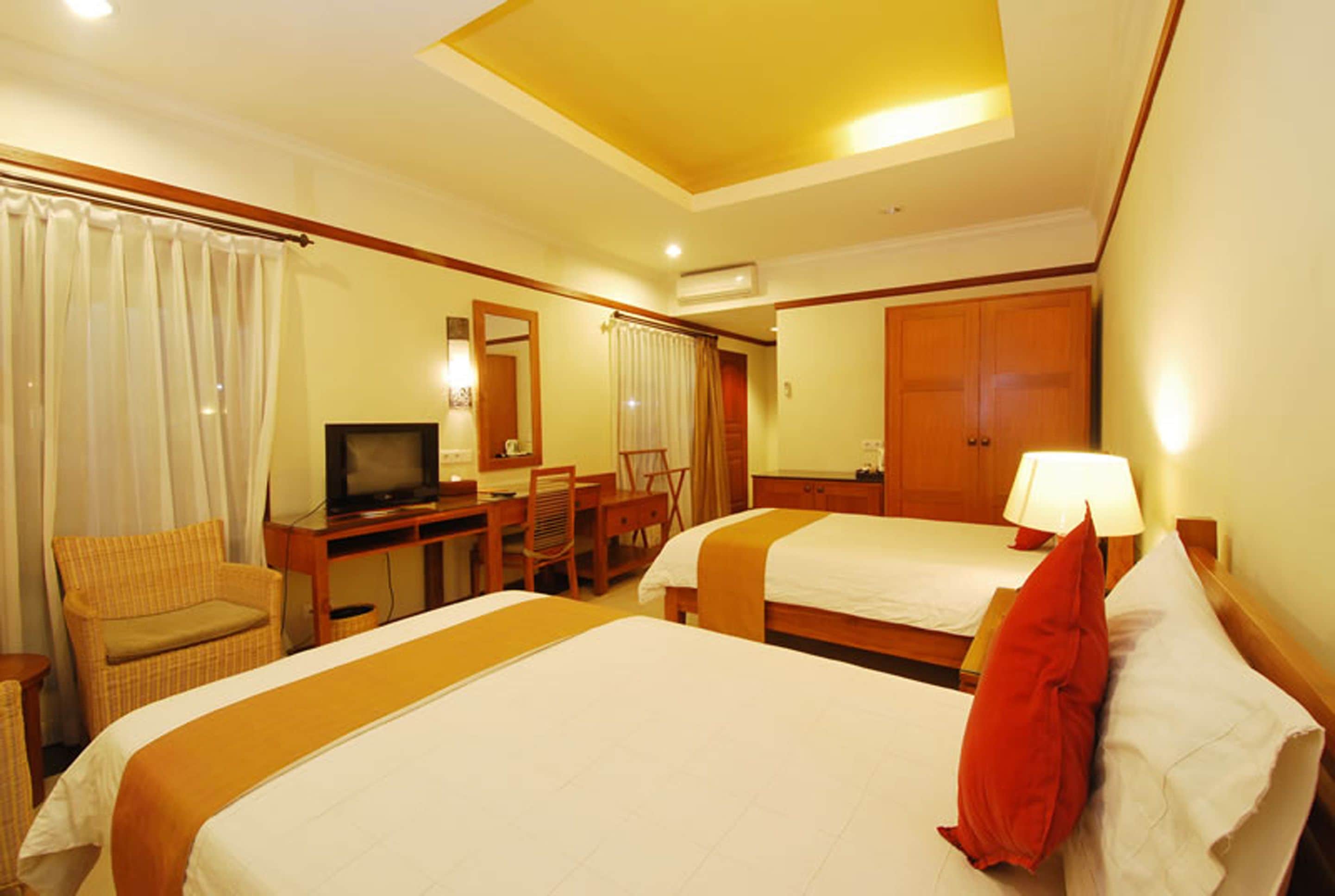 A hotel room with two beds, a desk with a television, a chair, and a wardrobe.
