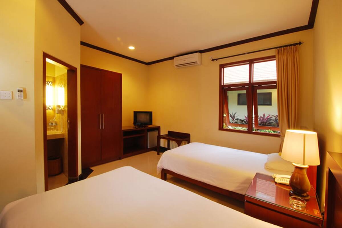 A hotel room with two beds, a TV, a desk, and a window with curtains.