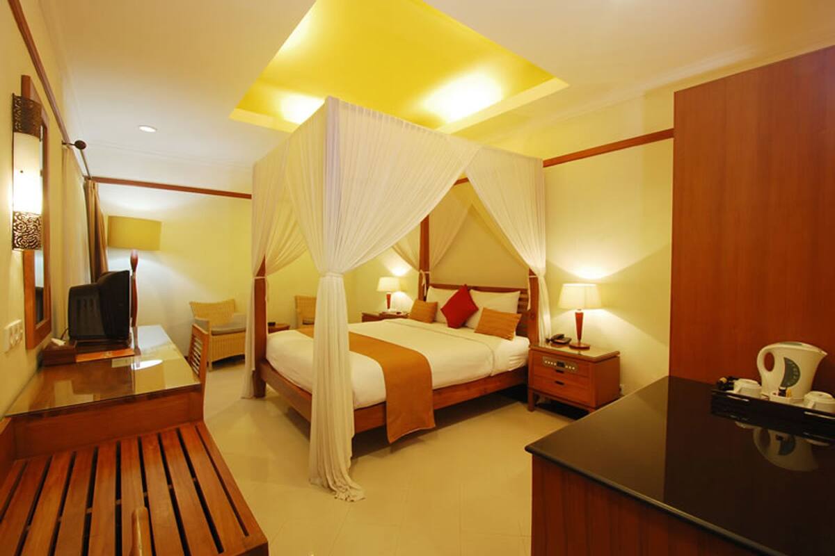 A hotel room with a four-poster bed, bedside tables, a desk, and a television.