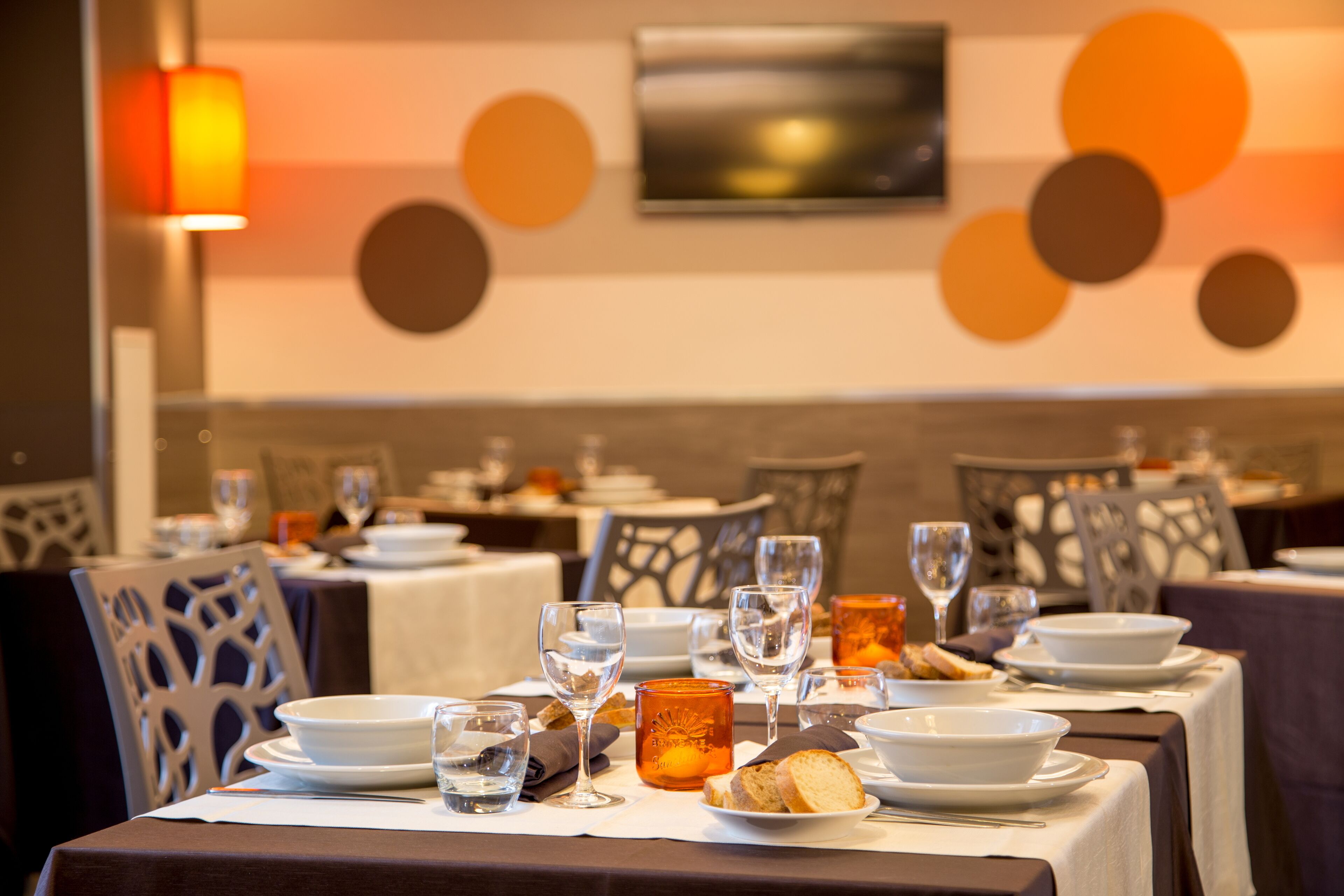 A restaurant interior with tables set for dining, featuring a modern decor with abstract wall art and a warm ambient light.