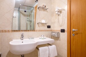 A bathroom with a sink, mirror, towel rack, and a shower area.