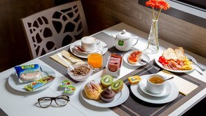 A breakfast table with various food items, a teapot, a vase with flowers, and a pair of glasses. - Hotel Domidea (Rome)