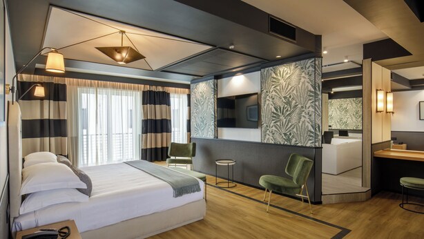 A modern hotel room with a large bed, a desk, a chair, and a mirror. - Hotel Domidea (Rome)