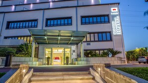 A modern hotel with a glass entrance, multiple floors, and a business hotel sign. - Hotel Domidea (Rome)