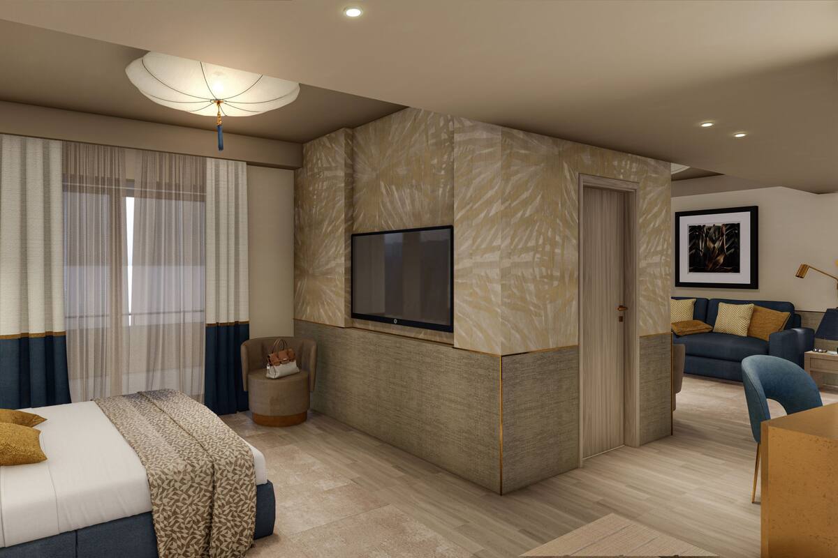 A modern hotel room with a bed, a TV mounted on a textured wall, a seating area with a sofa and armchairs, and a large window with curtains.