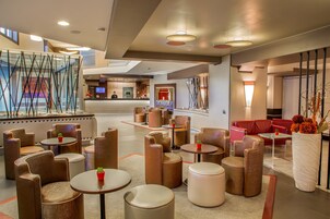A modern hotel lobby with seating areas, a reception desk, and a large vase with flowers.