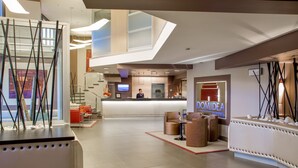 A modern hotel lobby with a reception desk, seating area, and a visible staircase. - Hotel Domidea (Rome)