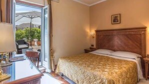 A hotel room with a bed, a desk, and a chair. There is a window with a view of the outdoors. - Tmark Hotel Vaticano (Rome)