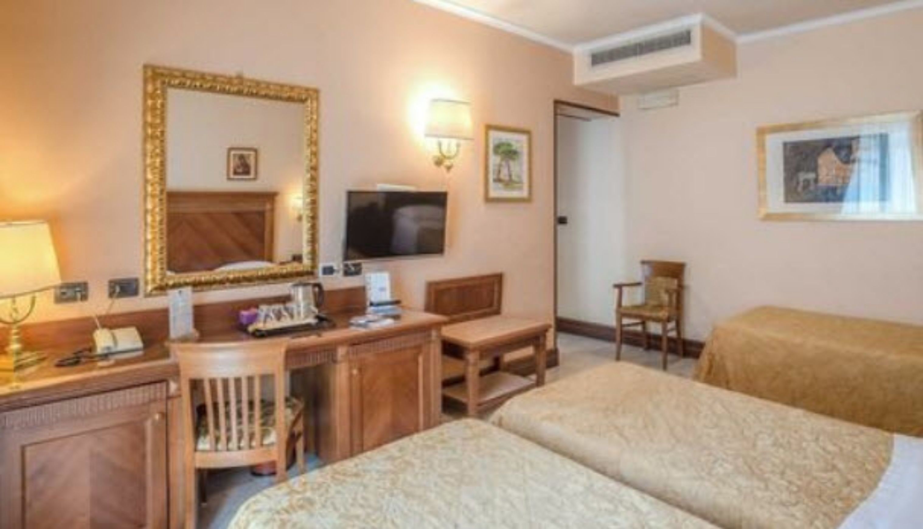 Habitación de hotel con dos camas, un escritorio con computadora, una silla, un espejo y un televisor.